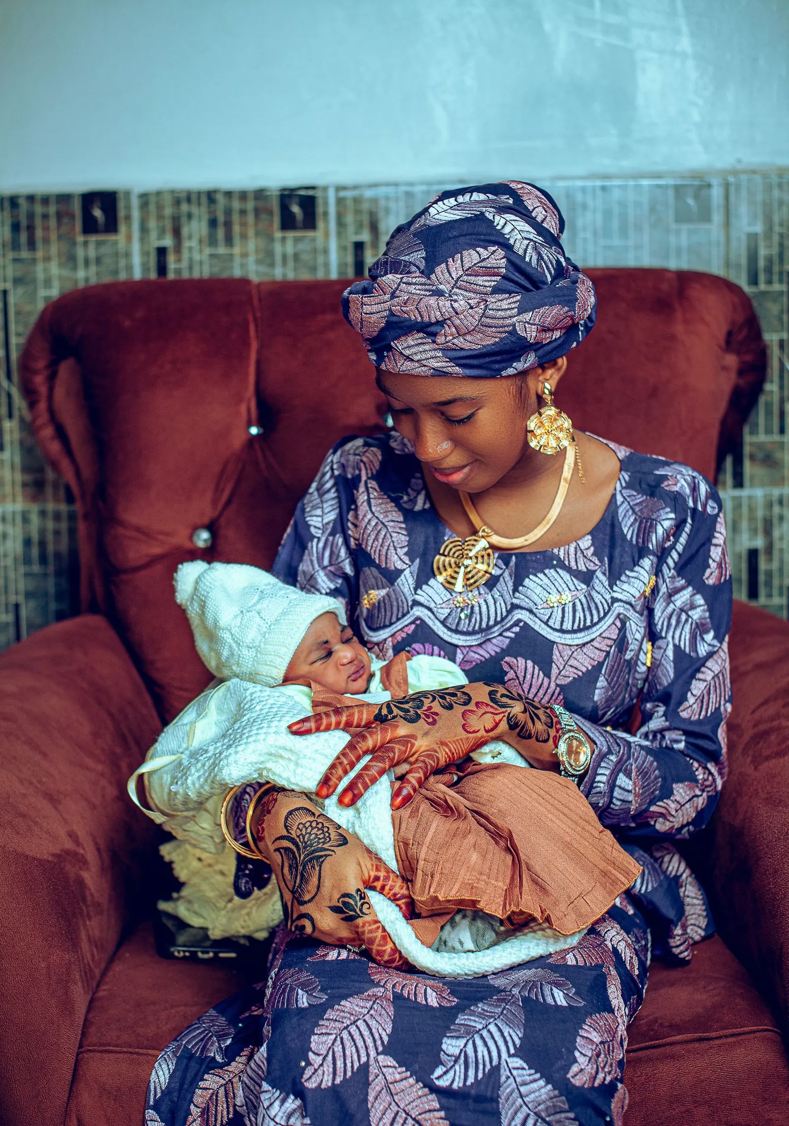 Mother in a patterned gown and headwrap cradling her newborn in an armchair
