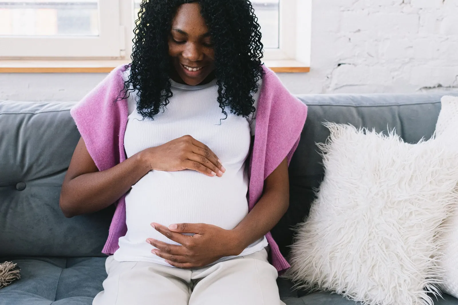 Smiling pregnant Black woman sitting on a sofa with her hands resting on her bump
